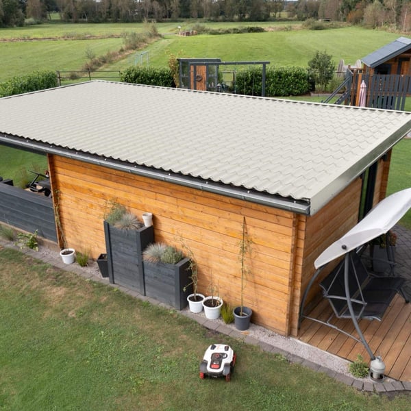 Dakpanplaat Grijswit op het dak van een lange houten schuur met terras in de tuin
