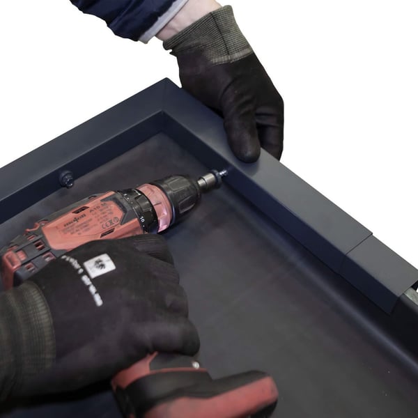 Montage van het antracietgrijze dakrandprofiel CUBE met schroeven en accuboormachine, handen zichtbaar