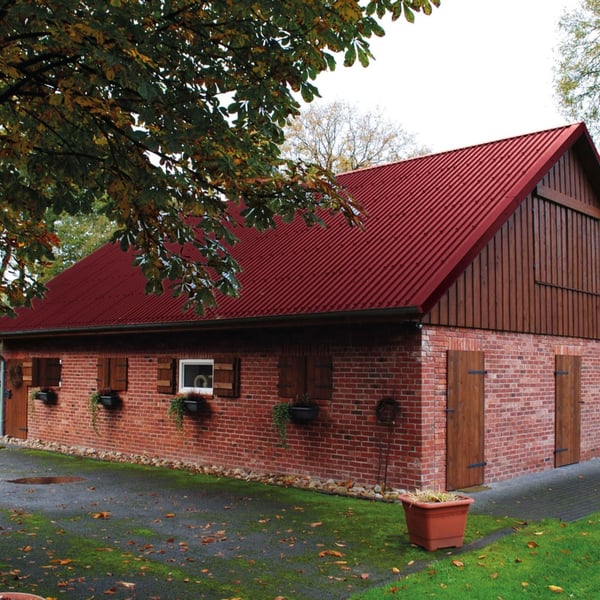 Damwandplaat 20/1100 wijnrood op het dak van een bakstenen gebouw met houten elementen