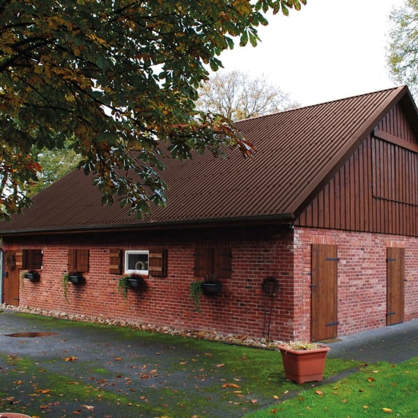 Damwandplaat 20/1100 in RAL 8017 op het dak van een bakstenen gebouw met houten aanbouw