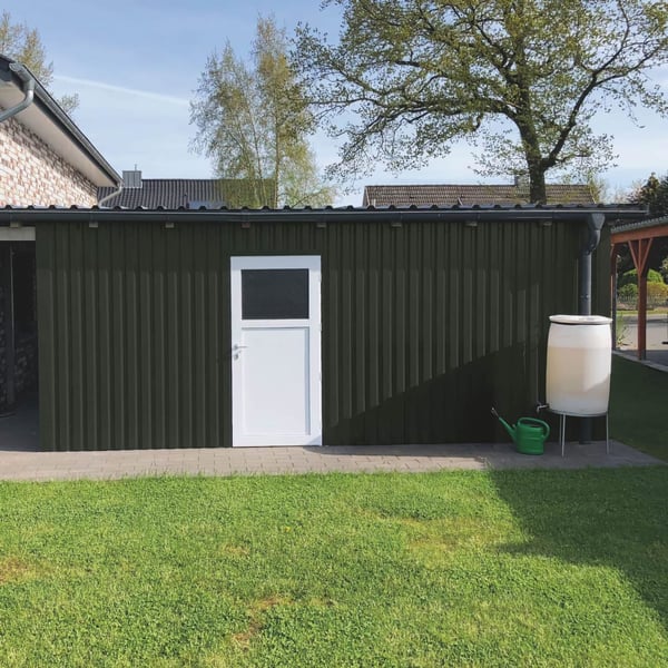 Damwandplaat 20/1100 wand chroomoxide groen als gevel van een garage met witte deur en regenton