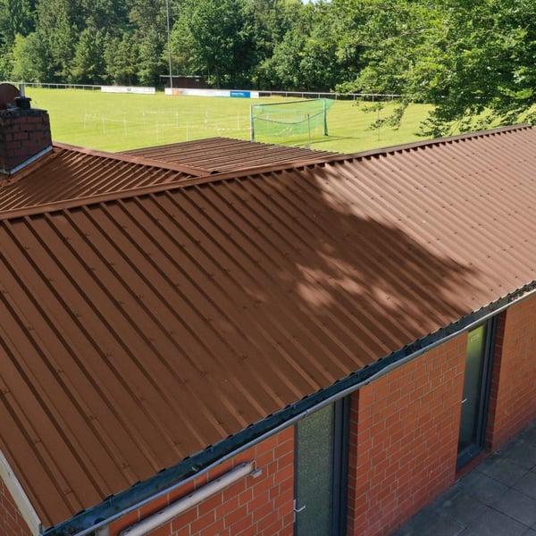 Damwandplaat 35/207 Notenbruin op een gebouwdak naast een sportveld