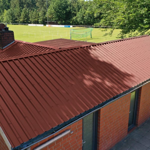 Damwandplaat 35/207 dak Roodbruin (RAL 8012) op een gebouw naast een sportveld