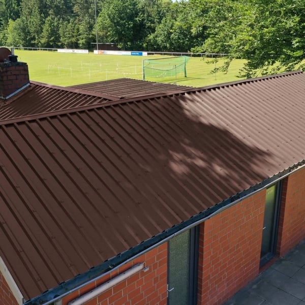 Damwandplaat 35/207, Chocoladebruin, als dak op een gebouw naast een sportveld