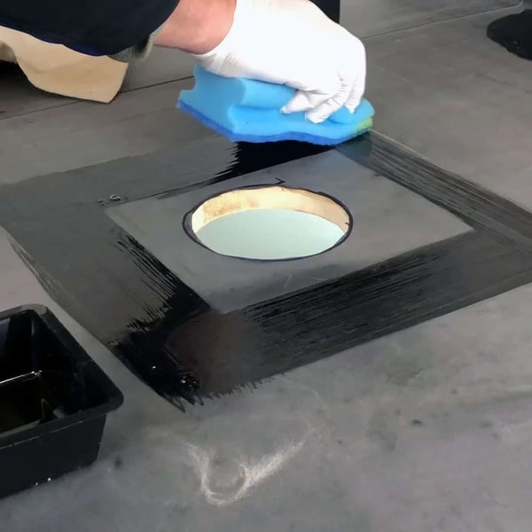 Montage van EPDM activering: Een hand met witte handschoen brengt zwarte vloeistof aan rond een dakafvoer