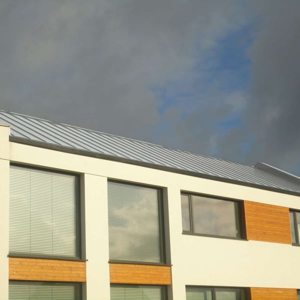 Modern gebouw met staande felsplaat PD-510-S Lichtgrijs (RAL 7035) dak onder bewolkte hemel