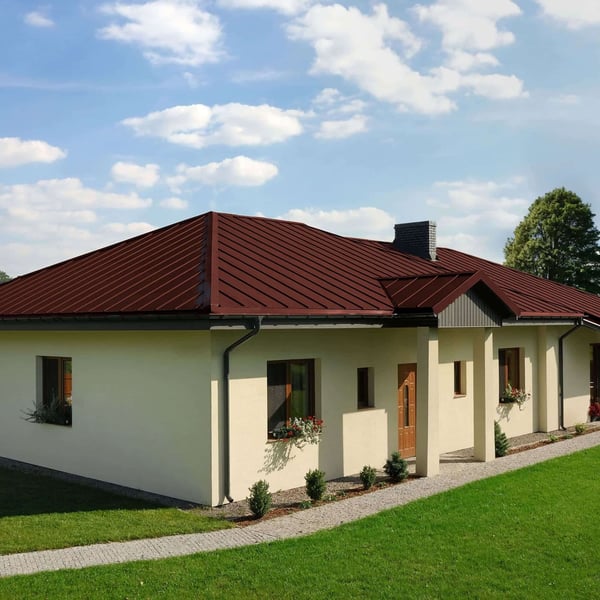 Staande felsplaat PD-510-S roodbruin op een bungalow met zadeldak en een schoorsteen, zonnige dag