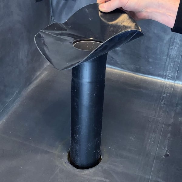 Hand houdt de zwarte EPDM garantie-gully boven de voorbereide opening in de dakbaan