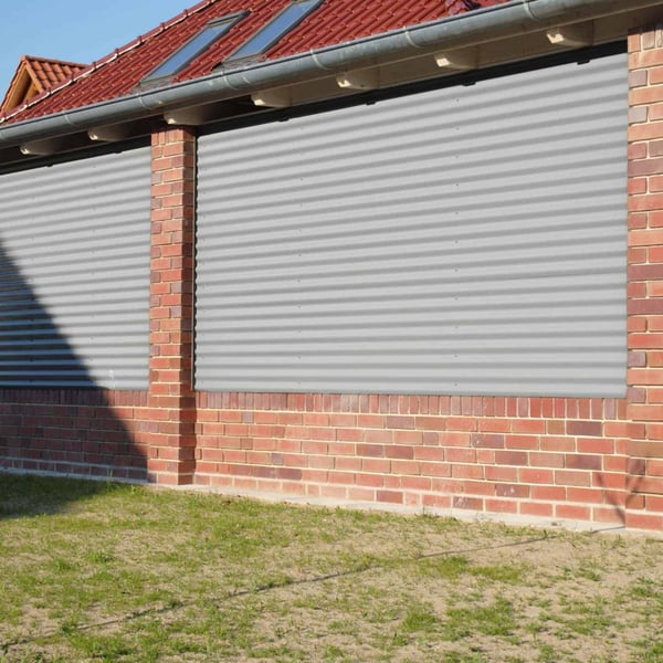 Golfplaat 18/1064, lichtgrijs, als wandbekleding tussen rode bakstenen pilaren van een gebouw