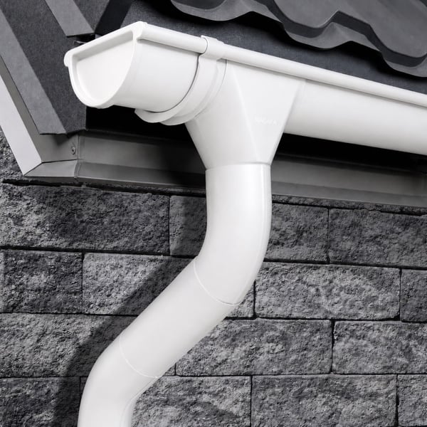 Witte dakgoot en regenpijp van Niagara, gemonteerd aan een huis met bakstenen muur en dakpannen