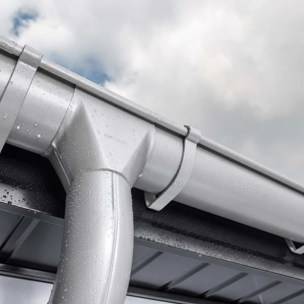 Detail van de rinnenablauf van staal in zilver-metallic (RAL 9006) met waterdruppels op een bewolkte dag