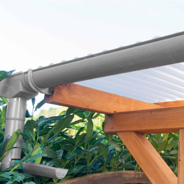 Grijze PVC-dakgoot met regenpijp en beugels aan een houten constructie