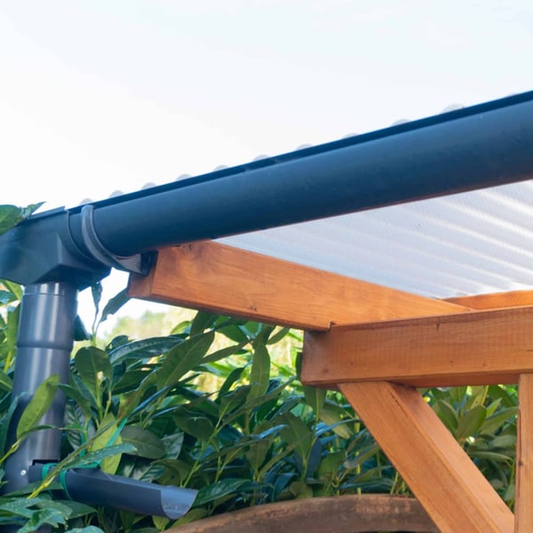 Grafietkleurige dakgoot met regenpijp aan een houten afdak met lichtplaten