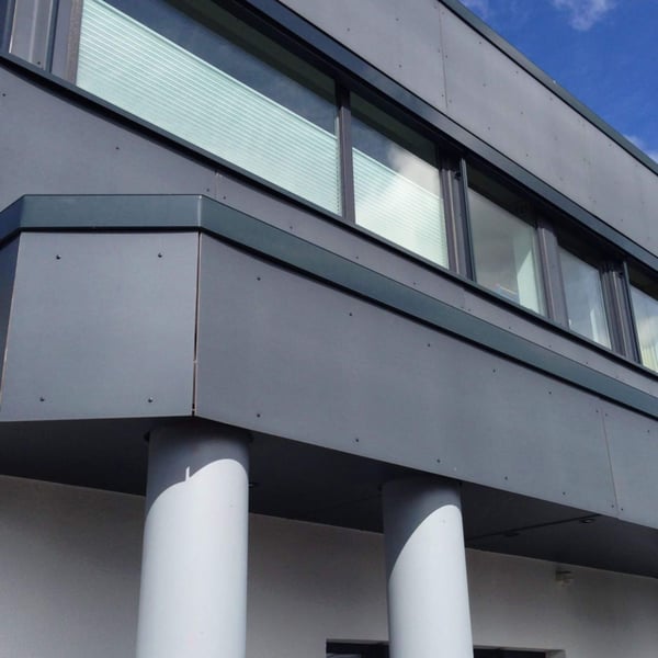Gebouwgevel met donkere HPL platen, ramen en twee zuilen op de voorgrond