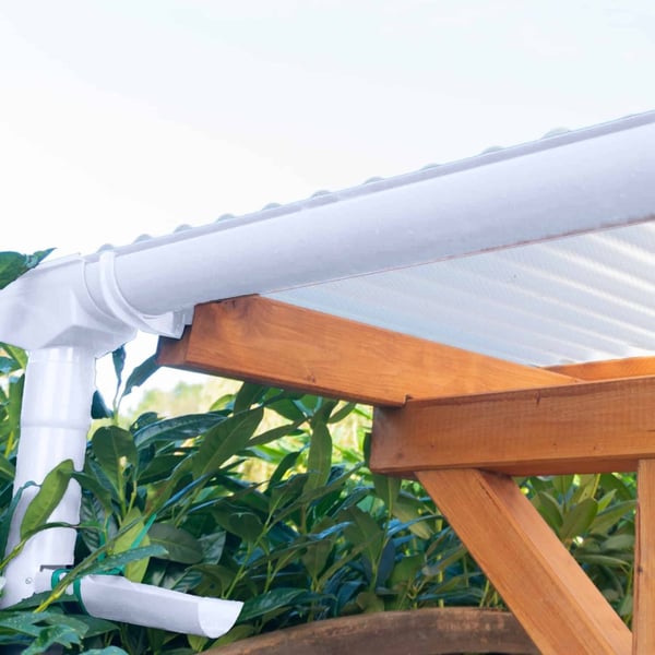 Gemonteerde witte PVC dakgoot en regenpijp aan een houten afdak met lichtplaten