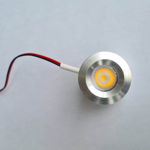 Detail van een enkele ronde LED lamp van blank aluminium, ingeschakeld met warmwit licht