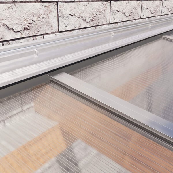 Wandaansluitprofiel van blank aluminium, gemonteerd aan een bakstenen muur boven lichtplaten