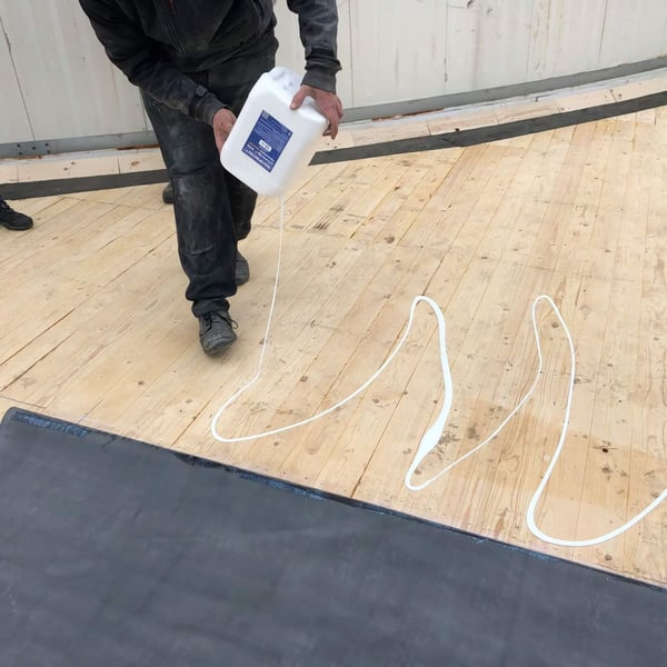 DACHPROTECT BlueTek oppervlakte lijm wordt uit de jerrycan in witte banen op houten dak gegoten