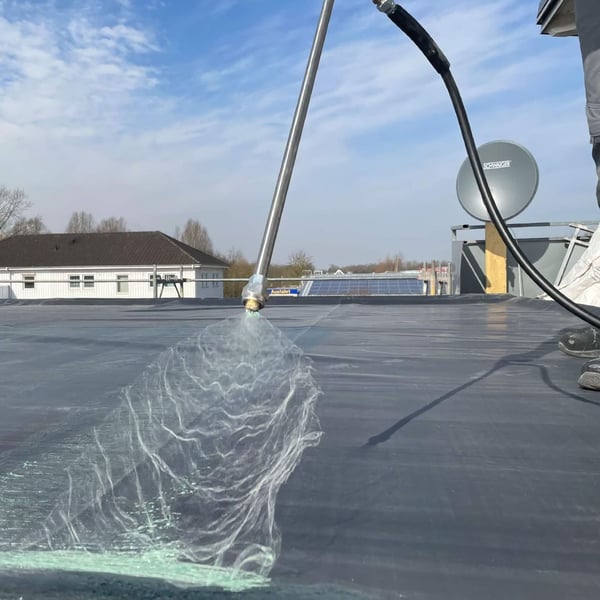 DACHPROTECT Spraybond 100 oppervlakte lijm wordt op een zwarte dakbaan gespoten
