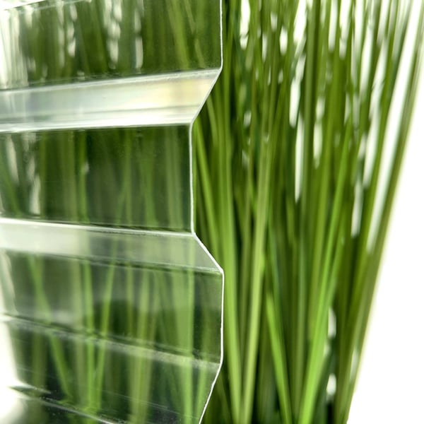 Detail van heldere PET damwandplaat 76/18 met groene planten op de achtergrond