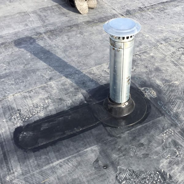 Detail van een geïnstalleerde zwarte EPDM buismanchet rond een ventilatiepijp op een plat dak