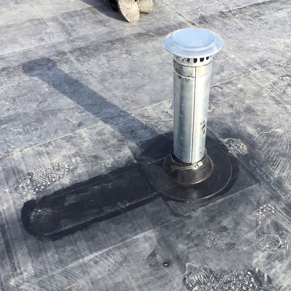 Detail van een zwarte EPDM buismanchet rond een metalen buis op een plat dak