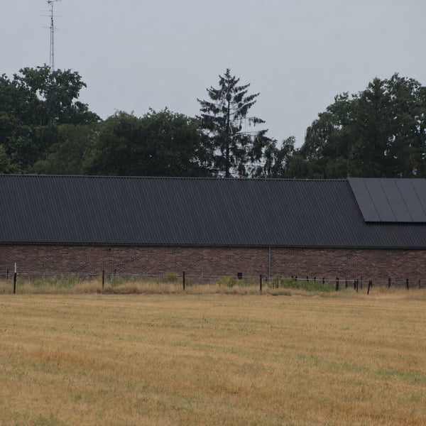Donkergrijze golfplaten van Stabipol op een langgerekt gebouw met bakstenen muur, verlegd