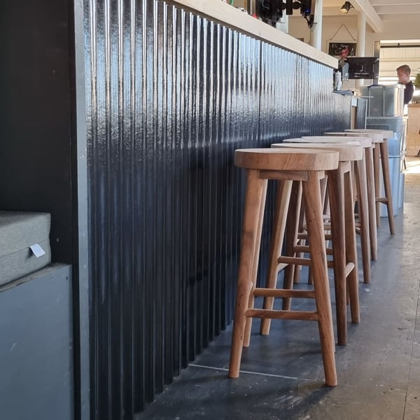 Donkergrijze golfplaten als wandbekleding van een bar, met houten barkrukken