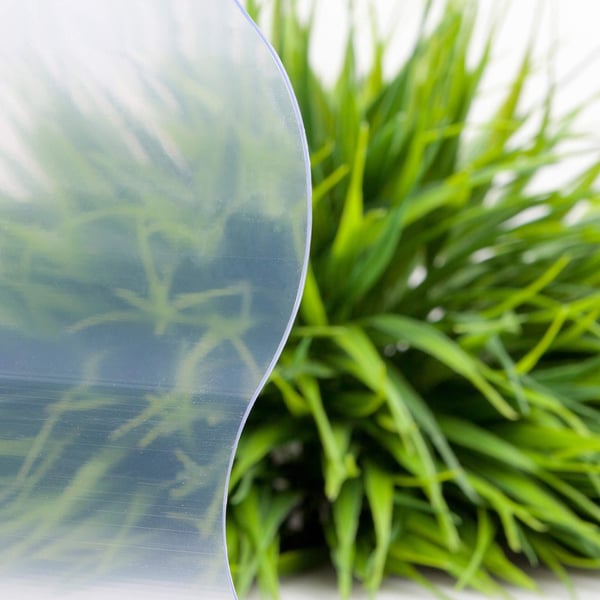 Detail van de lichtblauw getinte PVC golfplaat 177/51, 1,40 mm, met wazige groene achtergrond