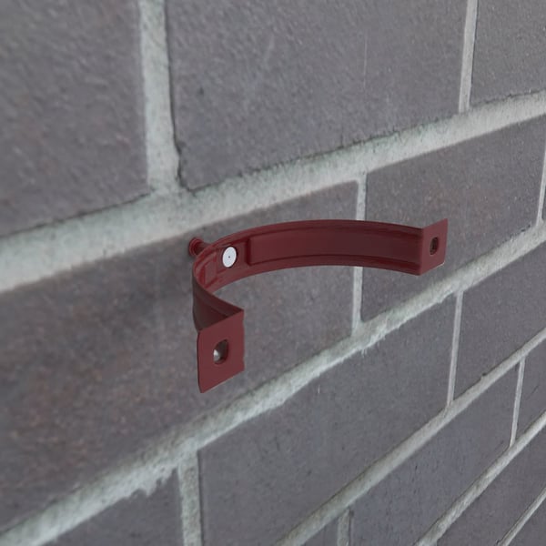 Kersrode stalen regenpijpbeugel gemonteerd op een bakstenen muur, met zichtbare schroef