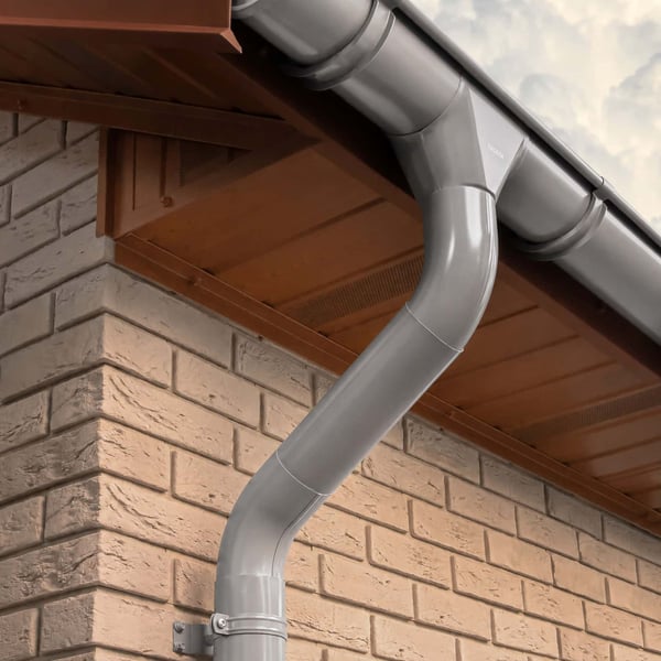 Grijs aluminiumkleurige dakgoot en regenpijp op een bakstenen muur, detail van installatie