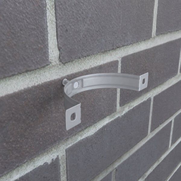 Enkele grijs aluminiumkleurige valbuisklem gemonteerd op een donkere bakstenen muur