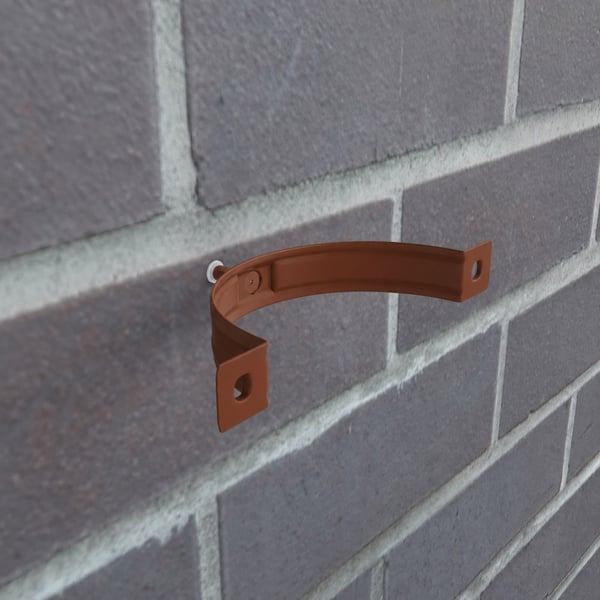 Enkele koperbruine (RAL 8004) valbuisklem gemonteerd aan een bakstenen muur, detail van bevestiging