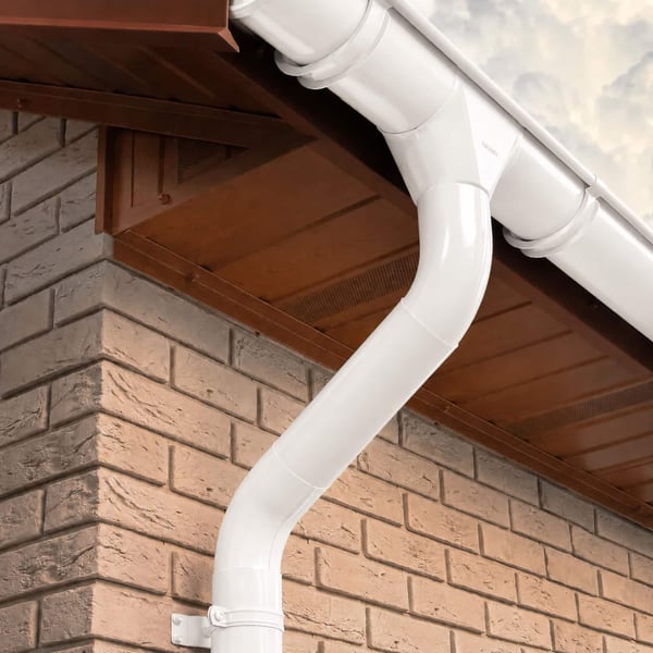 Detail van een zuiverwitte (RAL 9010) stalen regenpijp met bochten en beugels aan een bakstenen muur