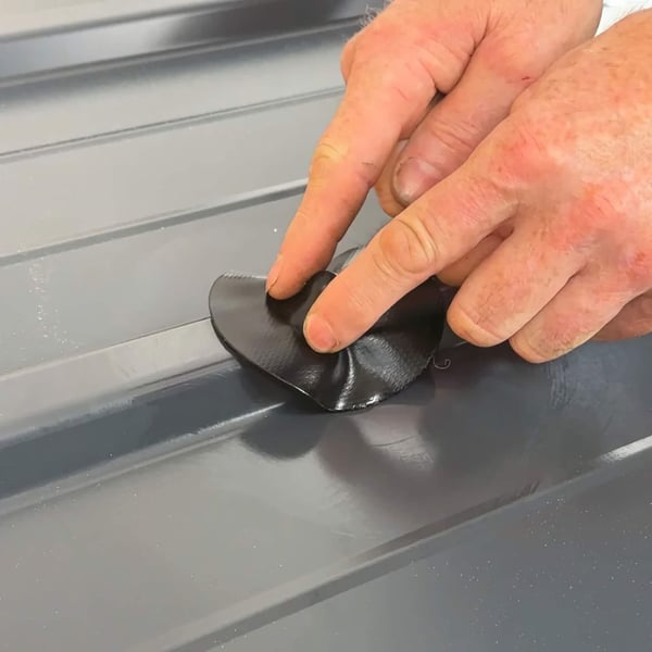 Handen drukken een zwarte EPDM schroef reparatiepleister op een profielplaat