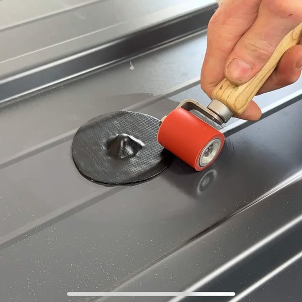 Hand rolt met een rode roller over een zwarte EPDM schroef reparatiepleister