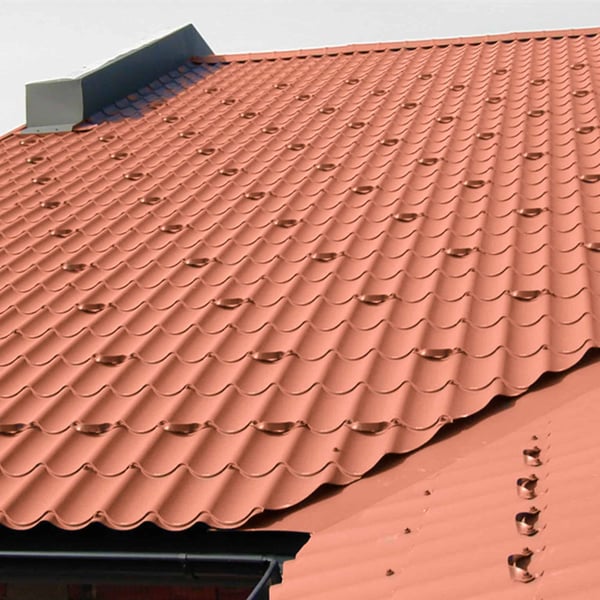 Dak met gemonteerde sneeuwvangbeugels in terracotta (RAL 8004) op dakpanprofielplaat