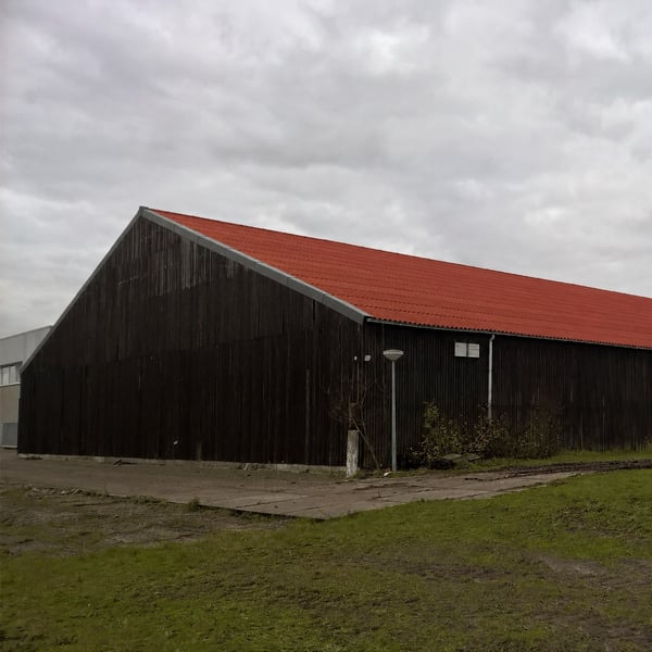 Vezelcement golfplaten 6,00 mm terracotta op het dak van een donkere houten schuur onder bewolkte hemel