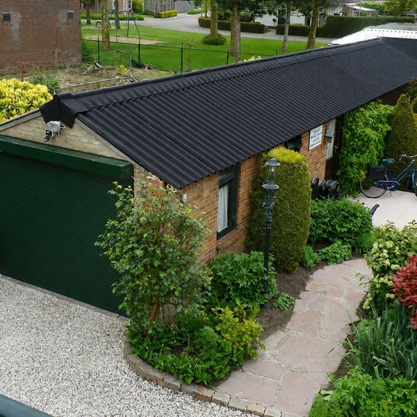 Zwarte golfplaten van vezelcement op het dak van een garage met groene garagedeur