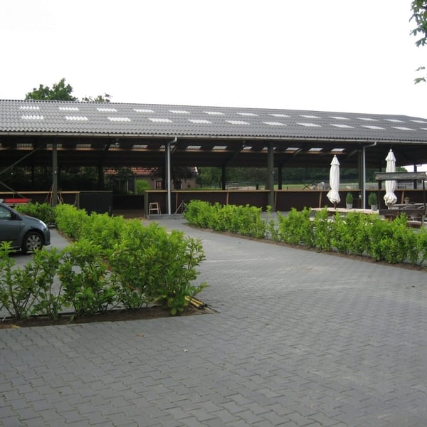 Open schuur met dak van zwarte golfplaten en witte lichtplaten, met geparkeerde auto
