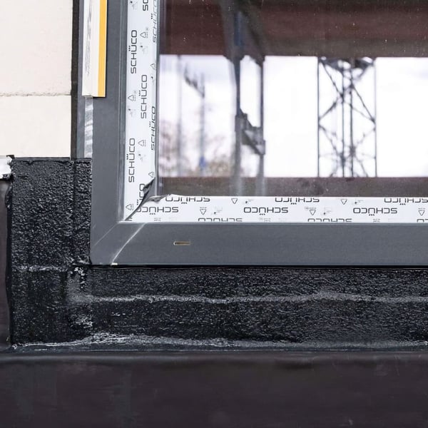 Detailaanzicht van een raamafdichting met zwarte vloeibare kunststof op een gebouwhoek