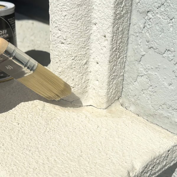 Vloeibaar kunststof transparant wordt met kwast aangebracht op een scheur in een witte, gestructureerde muur