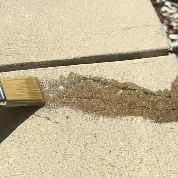 Transparant vloeibaar kunststof wordt met kwast op scheur in betonnen pad aangebracht