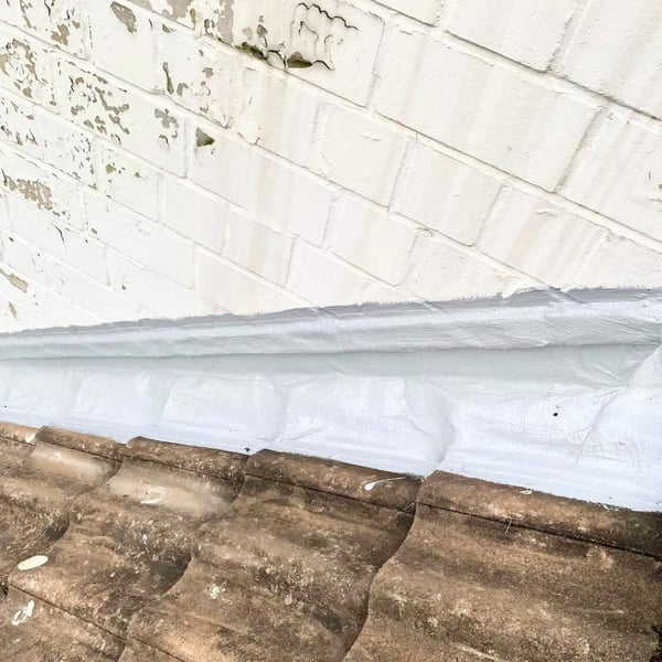 Dakafdichting met witte vloeibare kunststof aan een muur boven dakpannen