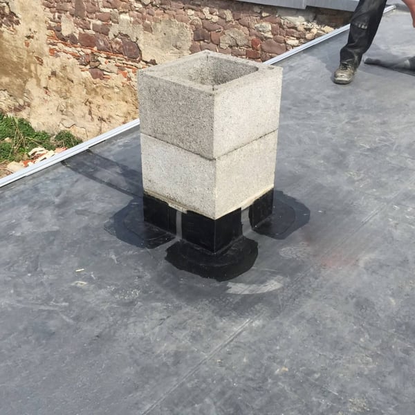 Plaatsing van het zwarte DACHPROTECT vorm- en afdekband van EPDM rond een betonnen schoorsteen