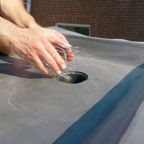 Handen plaatsen zilveren bladvanger in een dakgootgat op een donkere dakbedekking