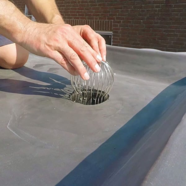Handen drukken zilveren bladvanger in een dakgootgat op een donkere dakbedekking