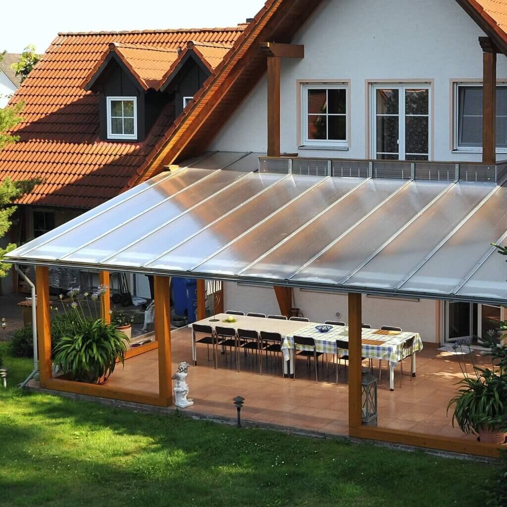 Er wordt een woonhuis getoond met een terrasoverkapping van kanaalplaten.