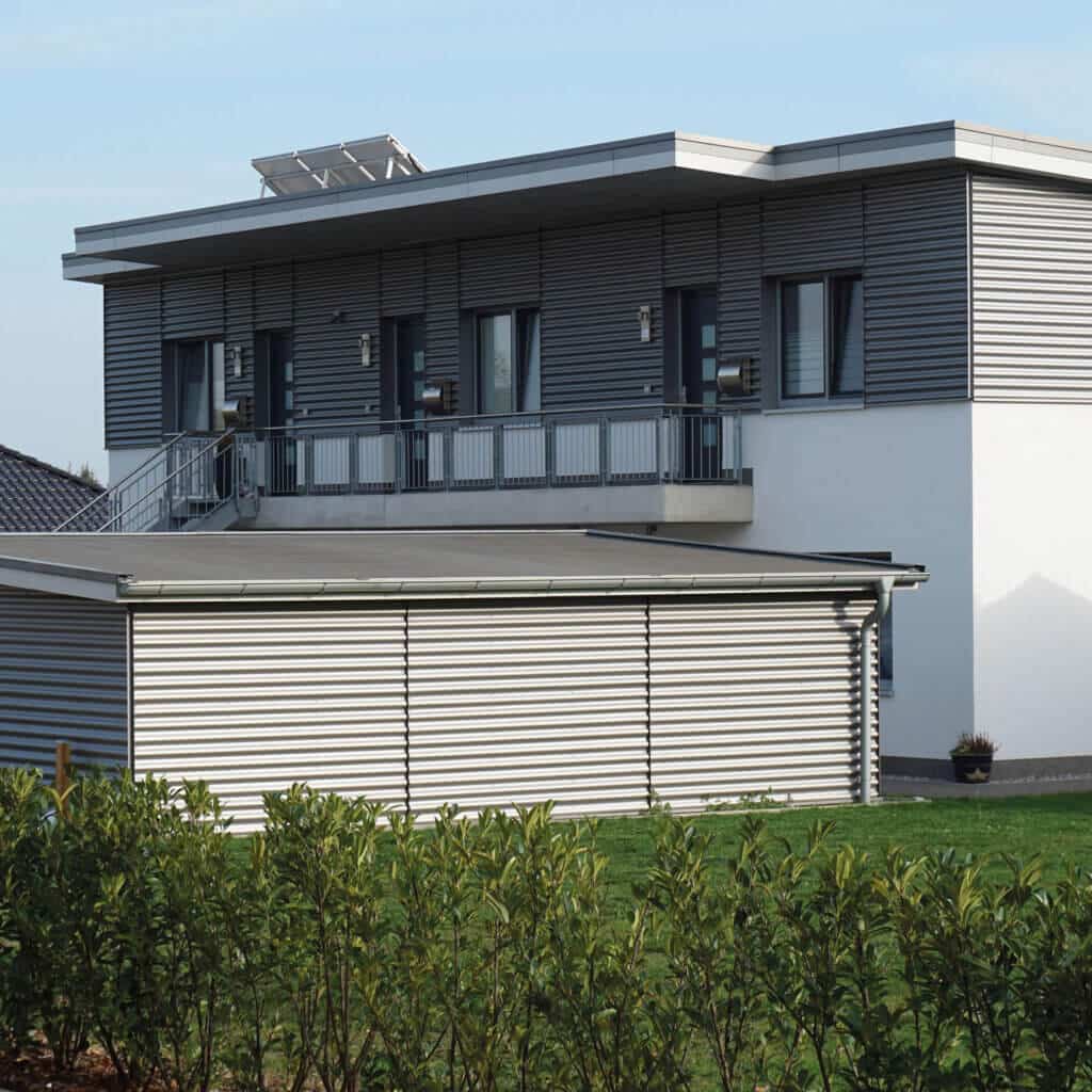 Er wordt een woonhuis getoond met grijze golfplaten als gevelbekleding.
