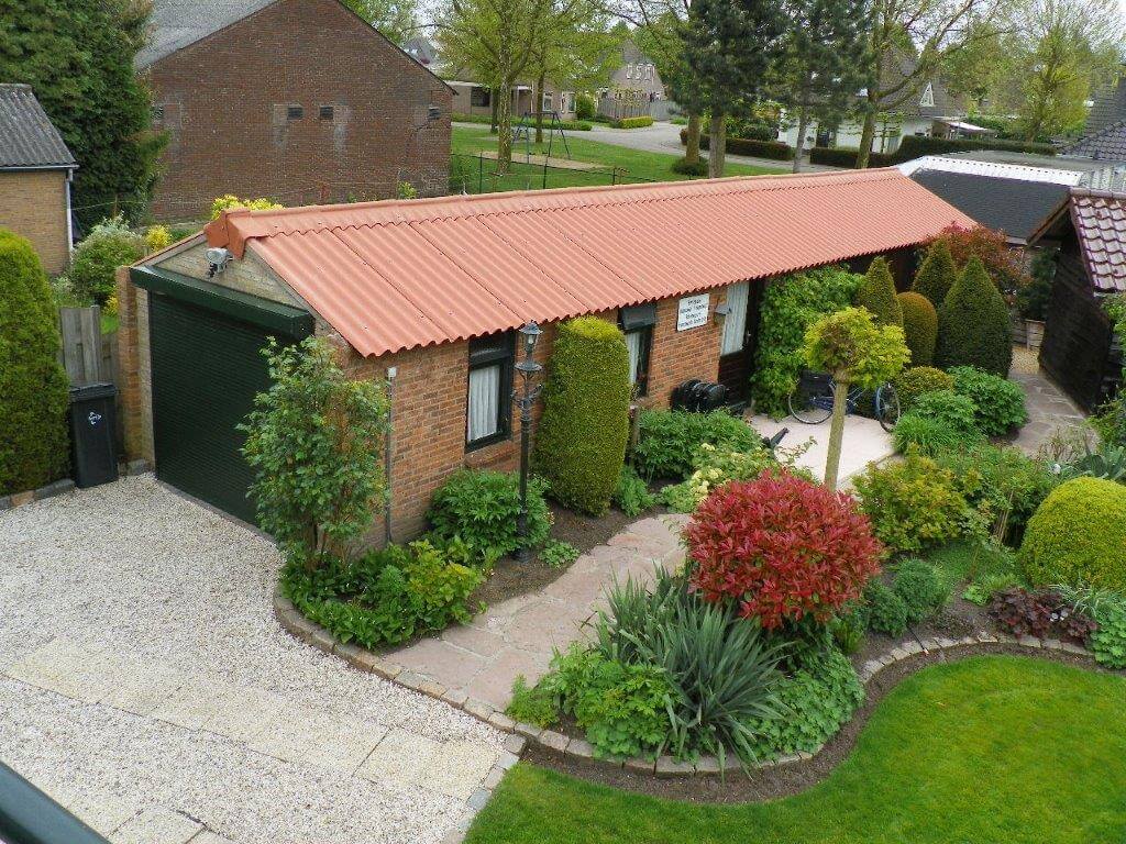 Een carport met een dakbedekking van rode vezelcementplaten, die duurzaam en weerbestendig zijn, aangevuld met een verzorgde tuin. Ideaal voor gebruik in particuliere woonomgevingen.